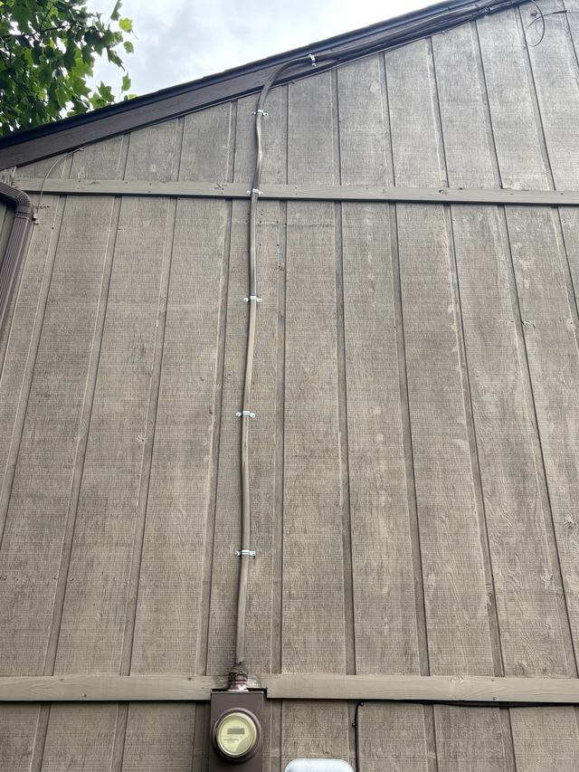 Electrical service cable clamped in a straight, tidy line down the side of a house to the meter